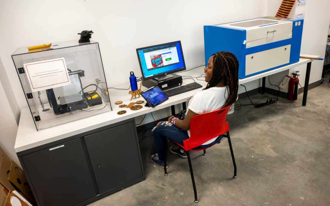 A student sits in a maker space, creating wooden objects.